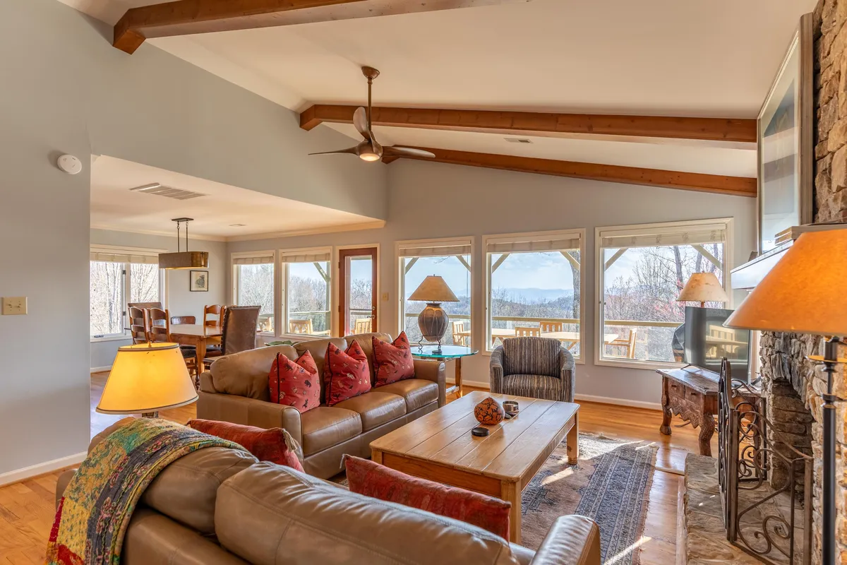 A warm and welcoming living room with a comfortable sofa, wooden coffee table, large windows offering scenic views, and a fireplace. The arrangement encourages family relaxation, entertaining guests, and shared experiences like game nights or reading by the fire.