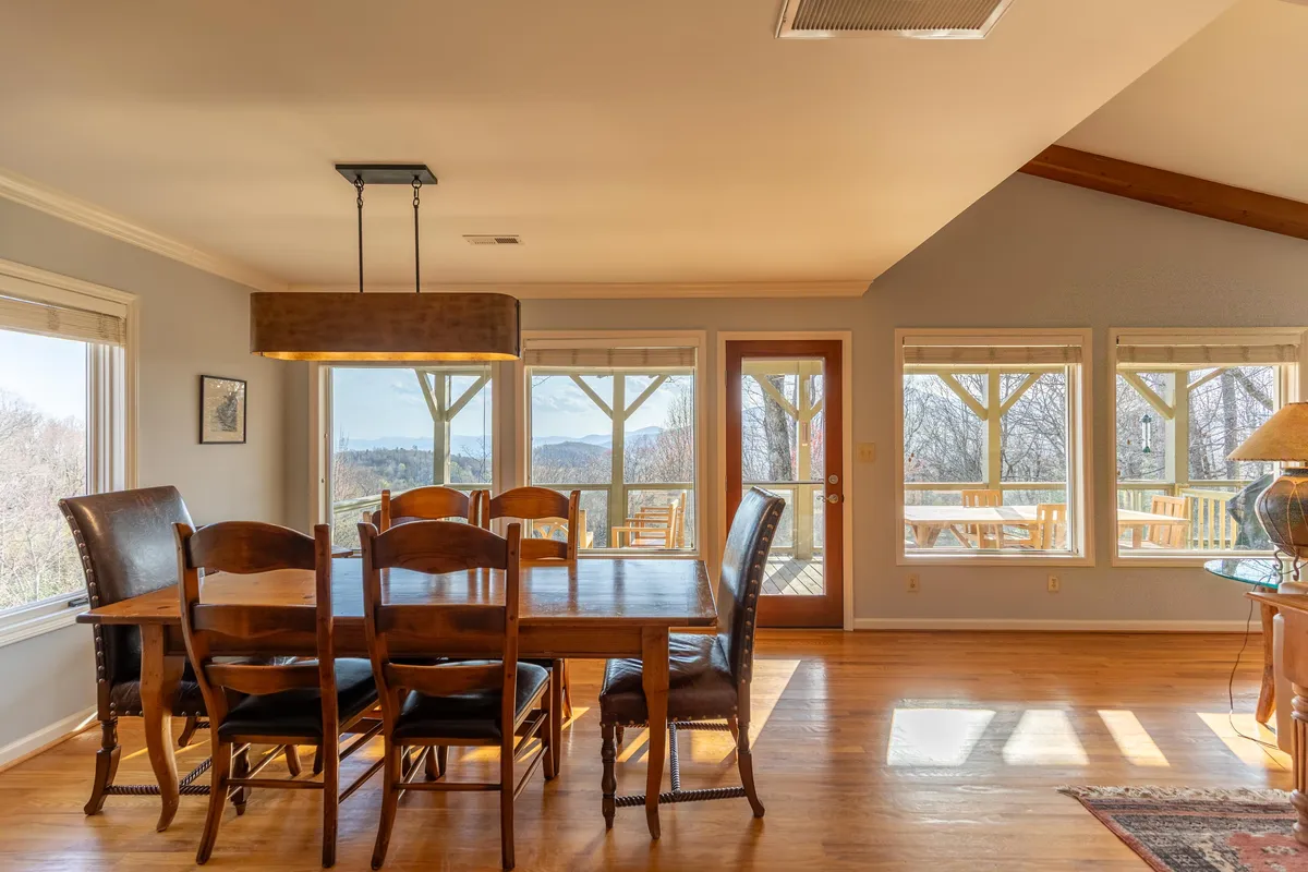 An inviting dining space with a large table, surrounded by comfortable chairs and illuminated by natural light streaming through generous windows. The views extend to the outdoors, suggesting a seamless flow between indoor and outdoor living spaces.