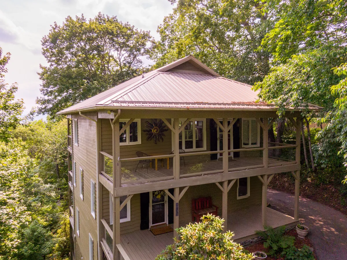 The image features a spacious balcony set amidst tall trees, highlighted by decorative wall art and a metal roof. The balcony offers ample room for relaxing or socializing while enjoying the fresh mountain air and natural surroundings.