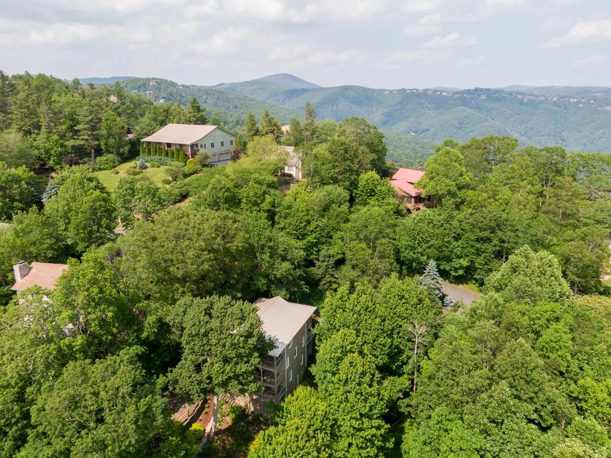 This image captures homes nestled among the trees with a stunning mountain backdrop and lush greenery, evoking the immersive natural setting that surrounds Sunset Vista and the Blowing Rock area. The peaceful mood and sense of scale highlight the proximity to the Blue Ridge Parkway and the abundance of hiking and exploration opportunities.