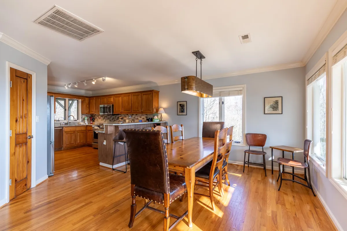 A spacious dining area seamlessly connected to a modern kitchen, with a large wooden dining table and chairs positioned beside expansive windows that offer breathtaking mountain views. The kitchen is equipped with high-end appliances and a generous granite island, creating a perfect space for sharing meals and socializing.