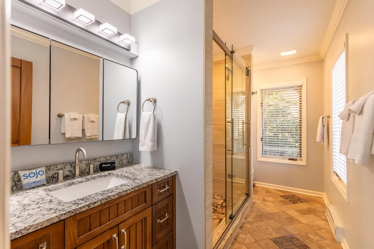A spa-inspired ensuite bathroom with a granite countertop, mirrored cabinets, and a glass shower enclosure. Sunlight streams in through a window, creating a tranquil and inviting atmosphere perfect for morning routines and relaxing self-care.