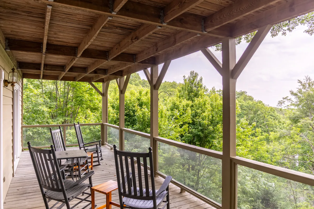 This exterior image captures a tranquil deck scene with inviting rocking chairs and a wooden table, all surrounded by lush green foliage and set behind a deck railing. The deck is oriented to showcase serene sunrise or sunset views, making it an ideal spot for relaxing, reading, or socializing while soaking in the sights and sounds of nature.