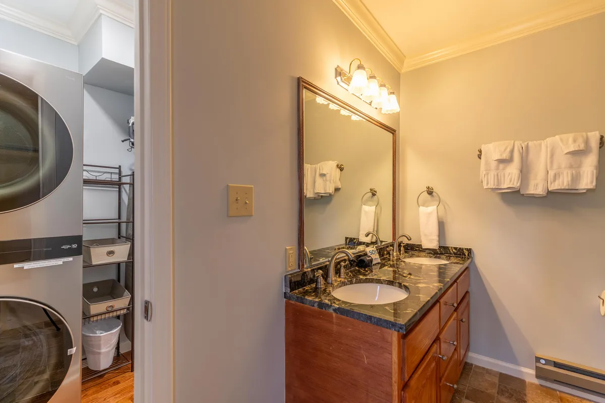 A spacious bathroom featuring a vanity with a large mirror, sink, towels ready for use, and laundry appliances nearby. The atmosphere is fresh, clean, and practical—ideal for shared use by families or groups.