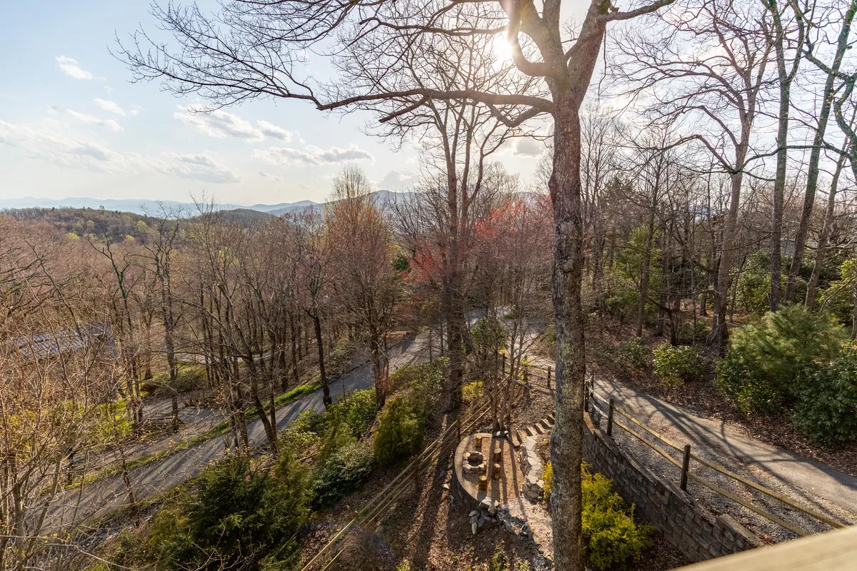 A scenic view of towering trees and winding pathways, with an outdoor seating area set in a forested environment. The scene evokes the ambiance of nearby trails and natural green spaces ideal for walks and exploration.