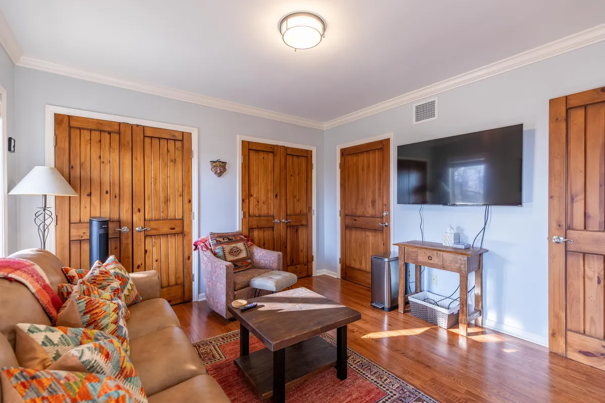 A warm, inviting living area with a comfortable sofa adorned with colorful cushions, wooden doors, and a modern television. The space feels homely and is suited for relaxation, watching TV, or gathering for board games and movie nights.